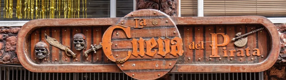 Aviso tallado en madera de La Cueva del Pirata con calaveras, sables y hacha pirata