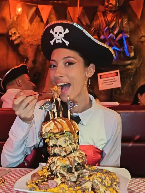 Clienta con sombrero pirata a punto de probar una hamburguesa gigante servida en torre