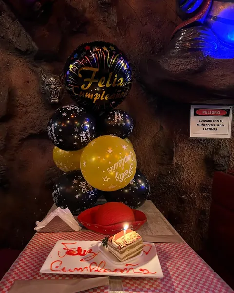 Mesa de cumpleaños con globos negros y dorados y una porción de torta servida