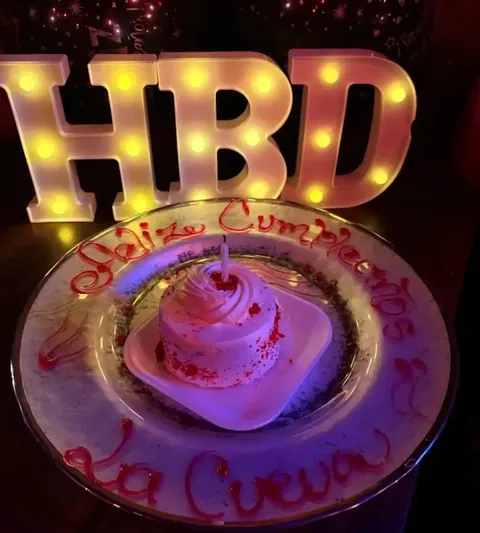 Torta de cumpleaños decorada a mano junto a letras luminosas HBD en La Cueva del Pirata