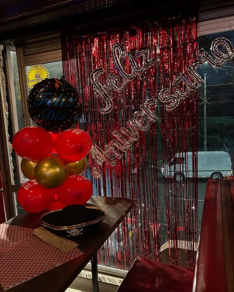 Montaje de aniversario con globos rojos y dorados y letrero luminoso de Feliz Aniversario
