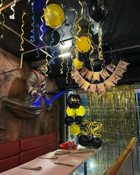 Zona de celebración montada con globos dorados y negros y cortina brillante detrás de la mesa